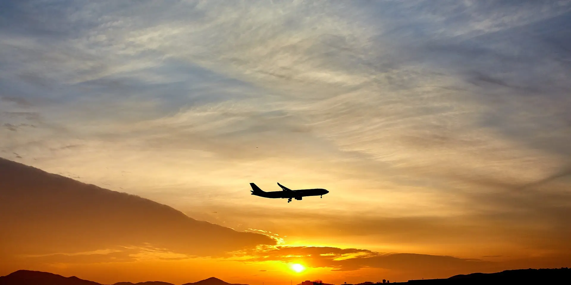An aircraft silhouetted against a golden sunset sky as it comes in to land.