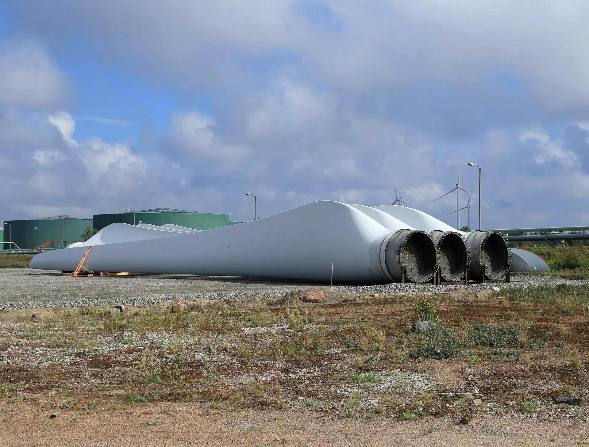 Wind turbine blades staged on supports at a port laydown area, with turbines turning in the distance.